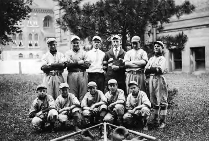 Group photo of the baseball team outside standing in front of some campus buildings.