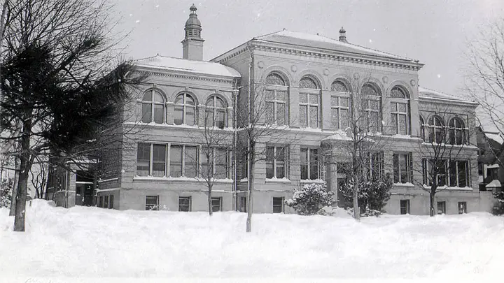 Black and white photo of a Beaux Arts, brick, 2.5 story building on a snowy, winter day.