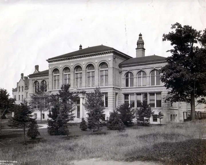 Black and white photograph presenting the building from a distance on a summer day.