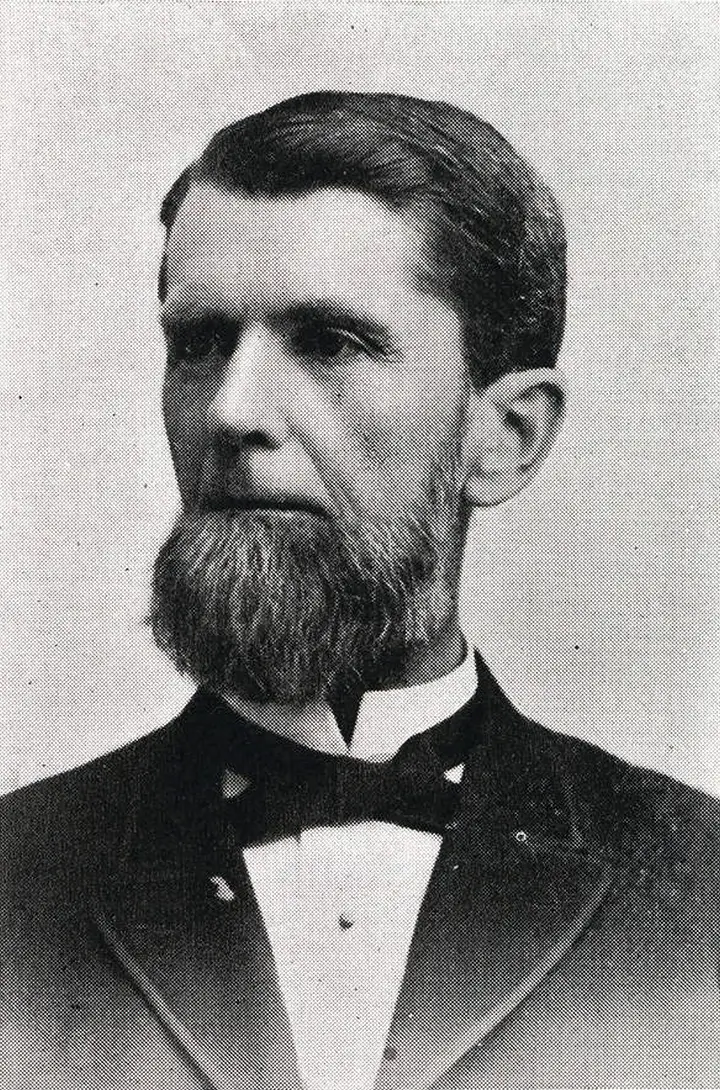 Black & white portrait of a middle-aged man wearing a suit and bow tie. He has a large bulbous beard with no mustache.