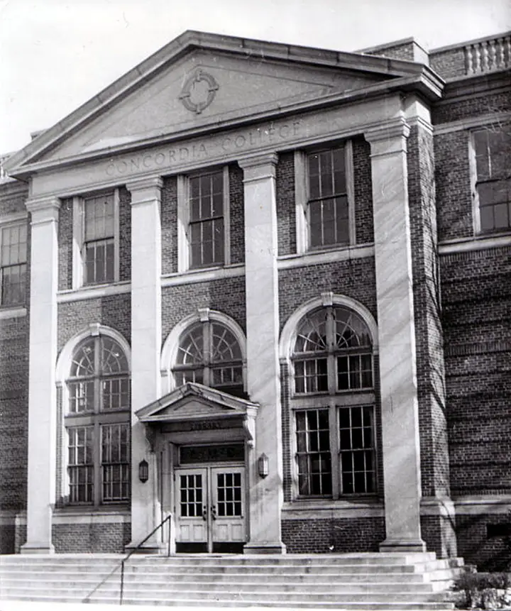 2 story brick college building with 4 limestone columns protruding from the building's face. Entrance is at the top of  stone stairs.