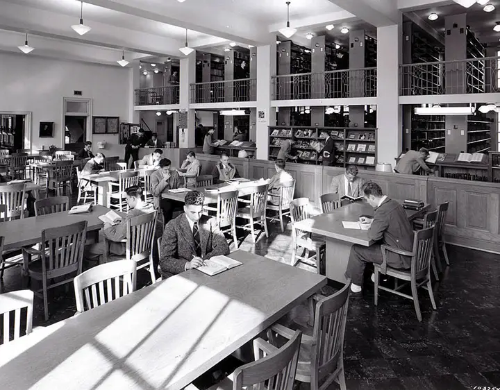 Tables at the front with students studying. In the rear are two floors of bookcases.
