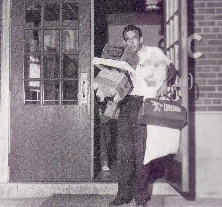 A man exiting a building with arms full of boxes and various other items.