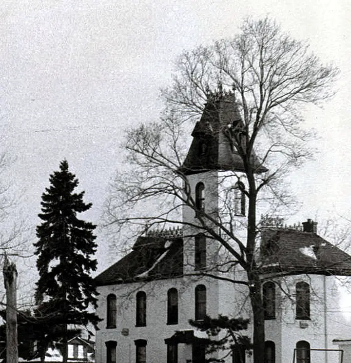 Black and white photograph of a two story house with a five story tower within.