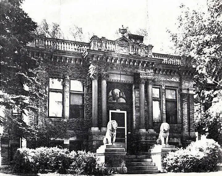 Old photo of an ornate, single story house with two stone lion statues on either side of the entrance.