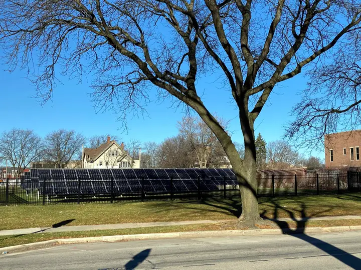 An array of solar panels on a grass lot with a surrounding fence.