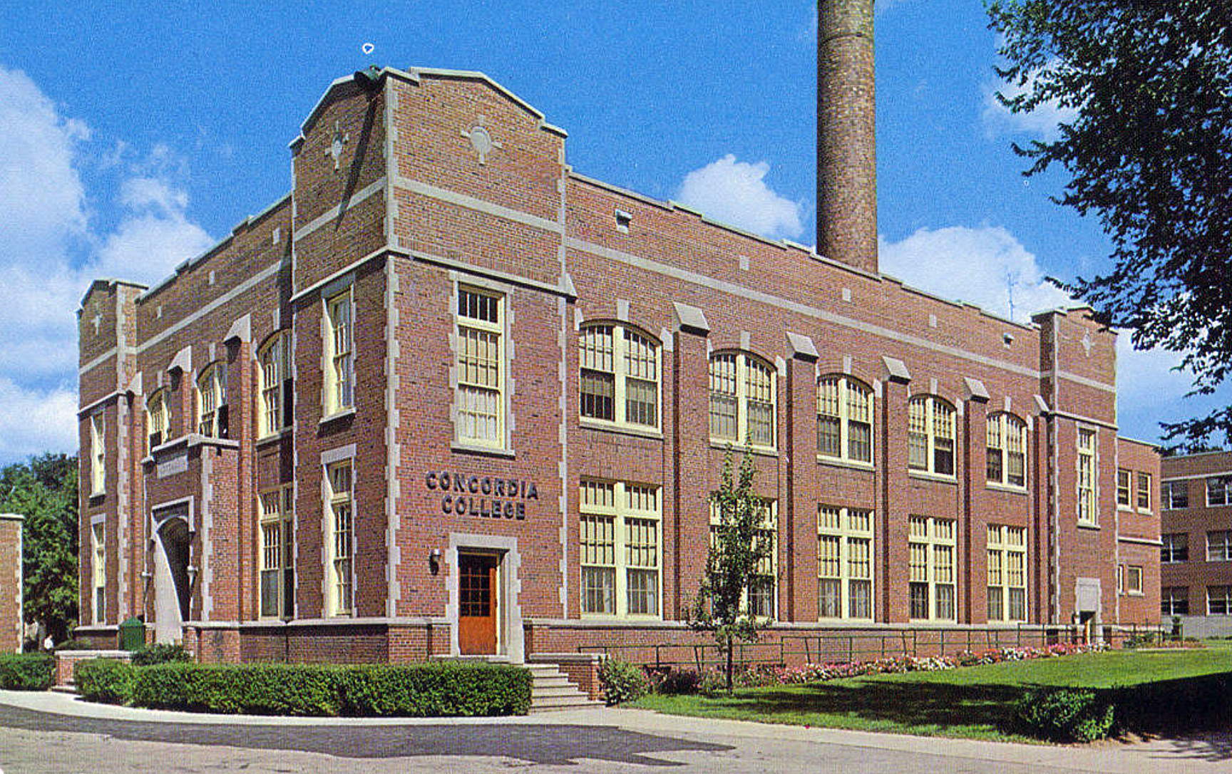 Two story brick refectory from an angle. A large smoke stack is visible on the roof. "Concordia College" in metal letters over the side entrance.