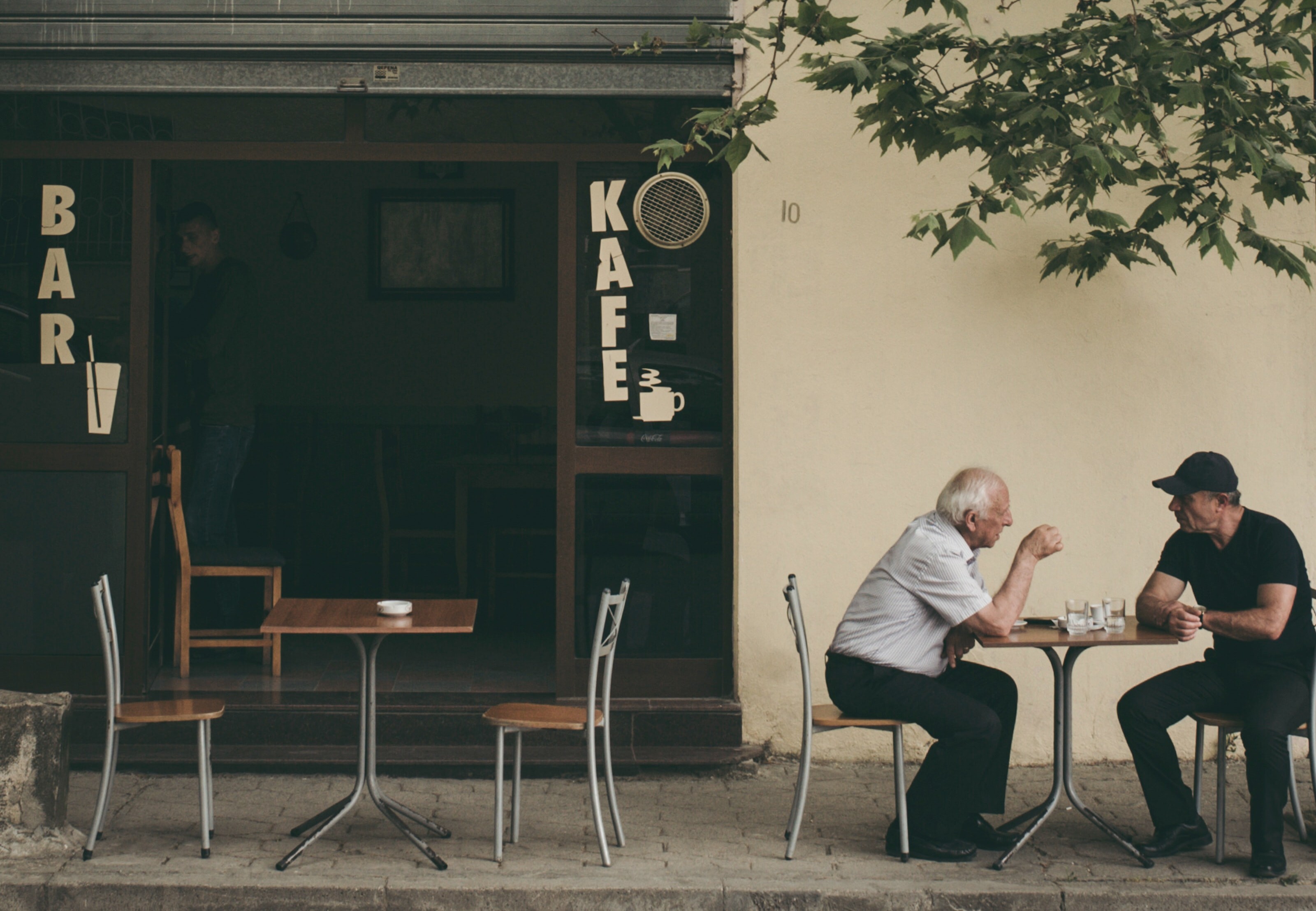 Two men talking outside of a bar/cafe.