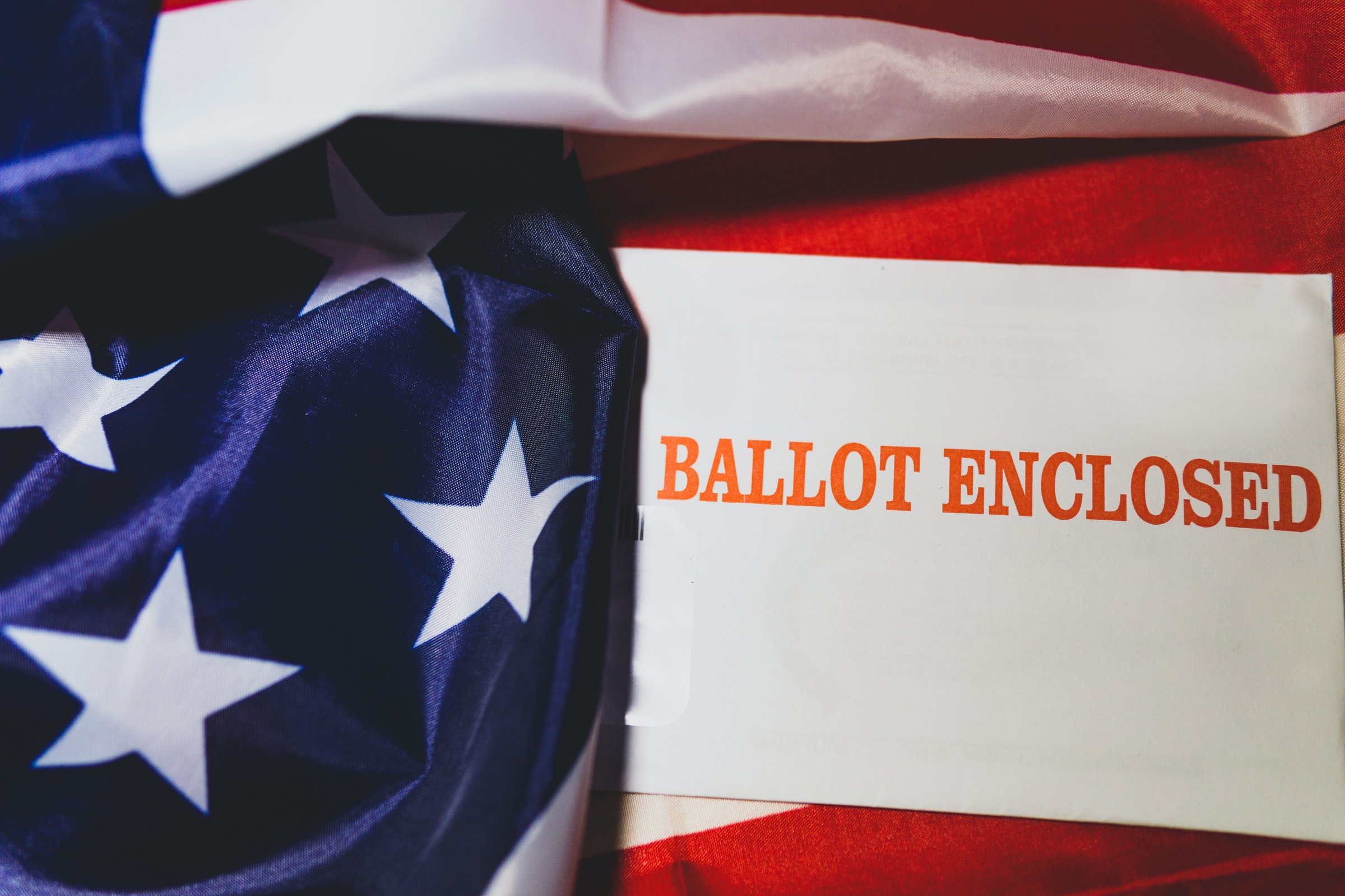 The stars from the American flag with a card laying on top of the stripes that says "BALLOT ENCLOSED" 