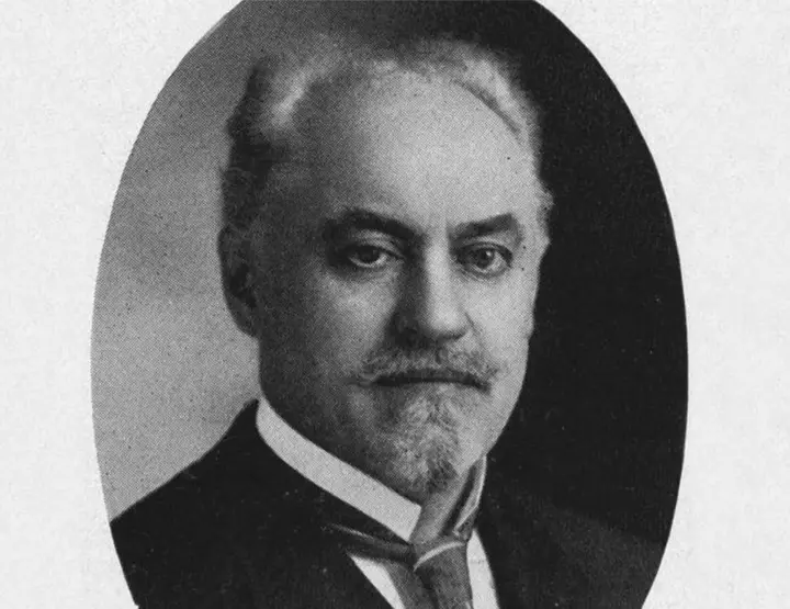 Black & white portrait of an elderly man wearing a suit and tie. His head is bald on top.