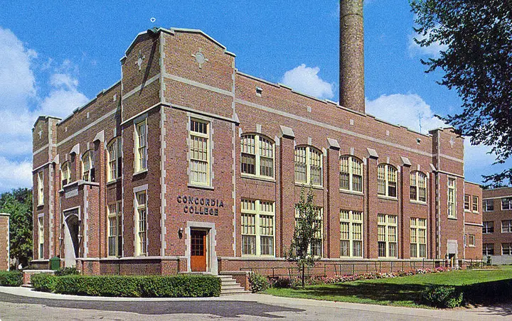 Two story brick building with a large smoke stack towards the back.