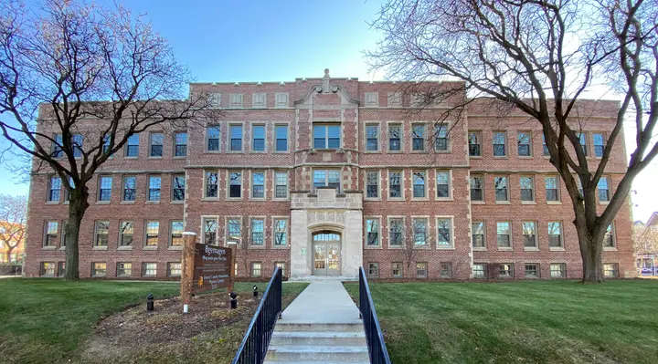 A picture of the front of the former Wunder Dormitory. Two leave less trees are in front of the building.