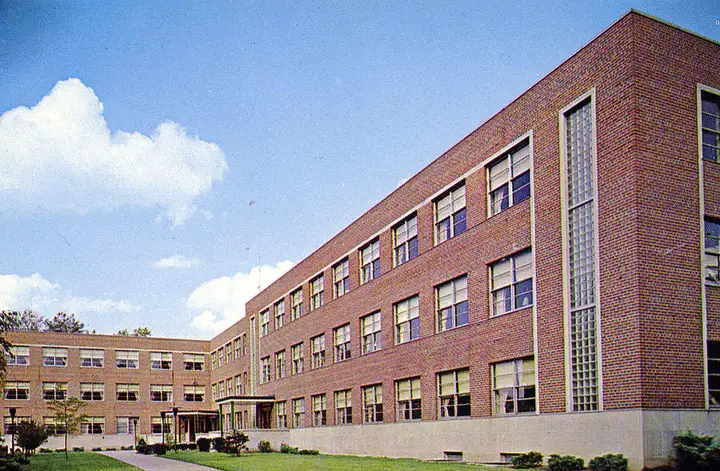 A 3 story L shaped brick building on a sunny summer day.