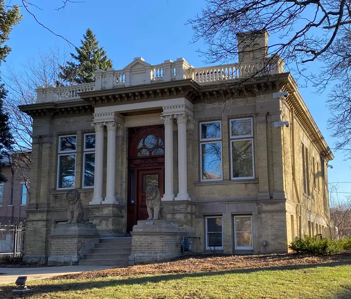 Current photo of an ornate, single story, cream city brick house with two stone lion statues on either side of the entrance.