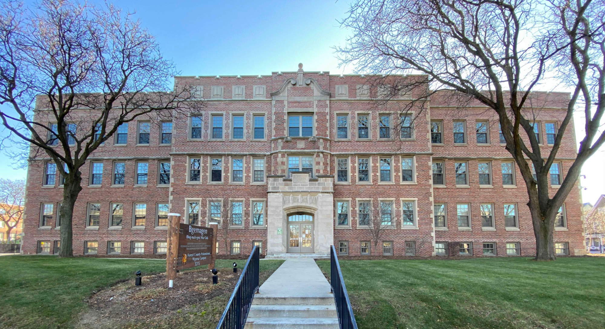 Old 3.5 story brick college building with leave-less trees flanking it in front.