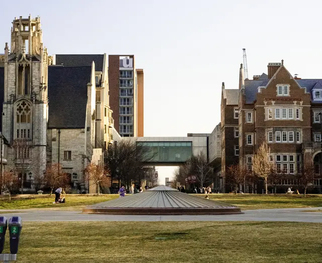 Students sitting in green grass at Marquette University with college buildings in background.