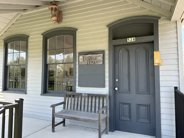 Front porch of original Town of Milwaukee Town Hall with a wood bench and old light fixture against clapboard wall.