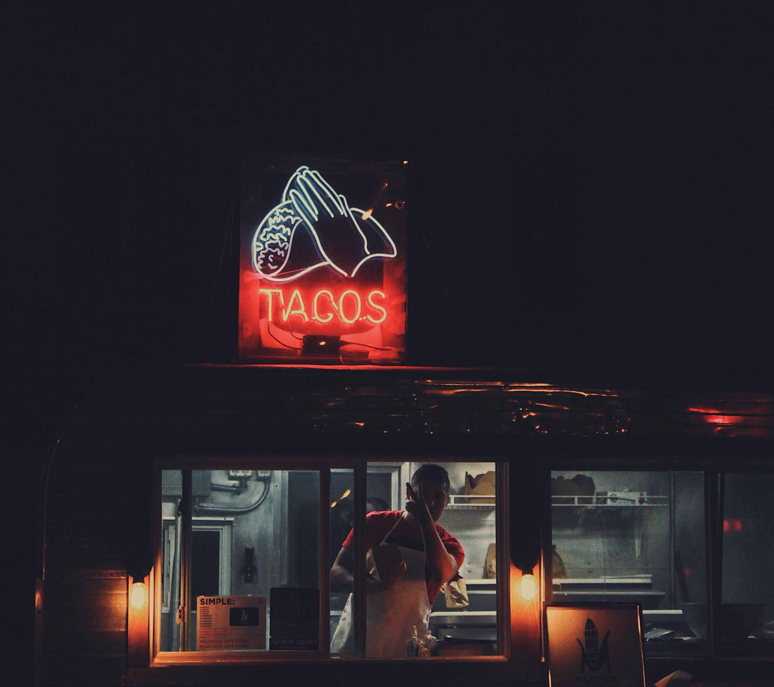 Food truck operator pointing up to the taco sign on his truck.